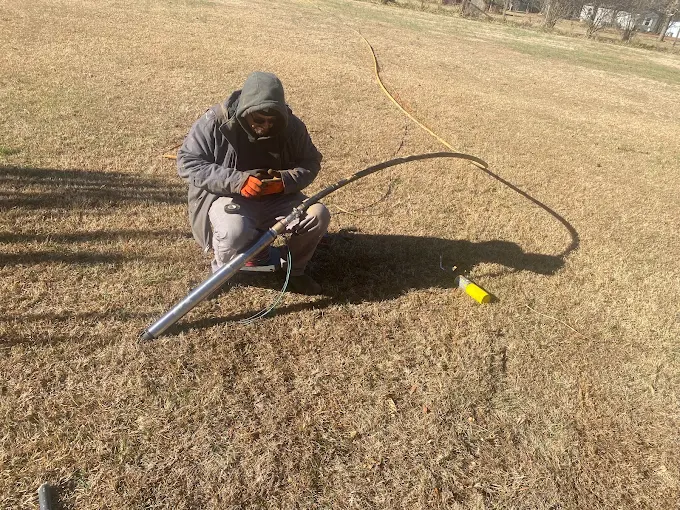 Technician wiring a submersible pump and poly drop pipe in an open field