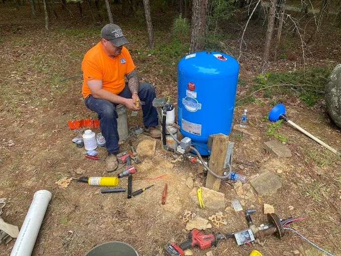 Shane in a Two Guys orange shirt setting a new blue pressure tank at an outdoor well