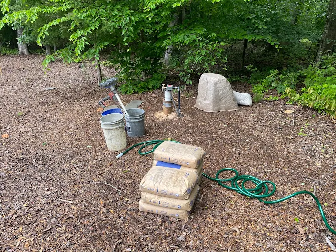Bags of well treatment and buckets staged beside a covered well head