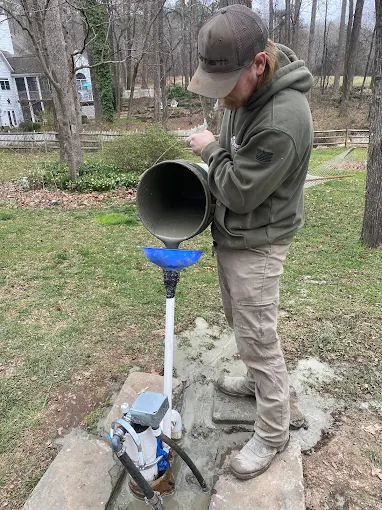 Pouring well treatment down the casing with a funnel at a home in Mebane