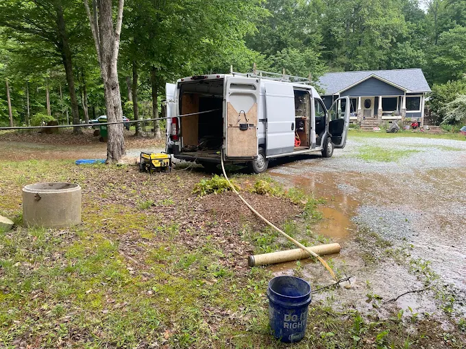 Two Guys service van at a country home with hoses run to a concrete well casing