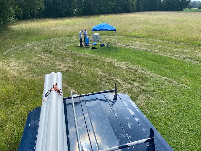 Well service in an open field with new PVC drop pipe loaded on the van's roof rack