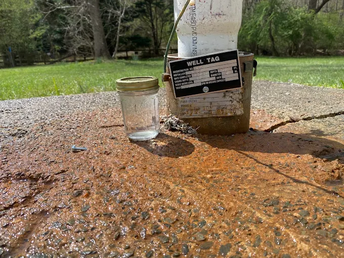 Jar of well water next to the official tag on a well casing