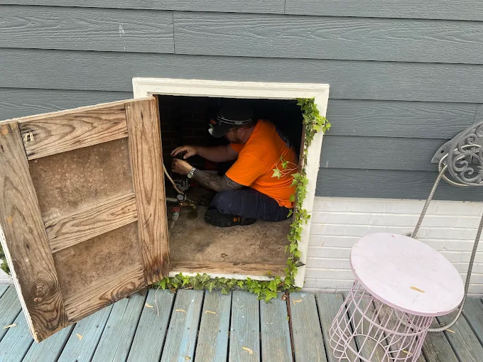 Technician working inside a crawl space access on well plumbing