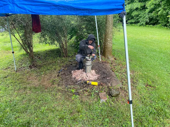 Technician servicing a well head under a canopy in the rain