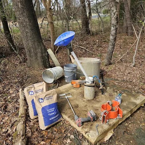 Tools, treatment, and buckets laid out around a well cap in the woods