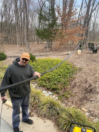 Shane pulling drop pipe up out of a well by hand on a wooded lot