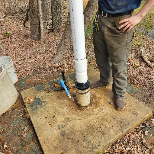 Fresh PVC drop pipe connected at the well casing on a concrete slab