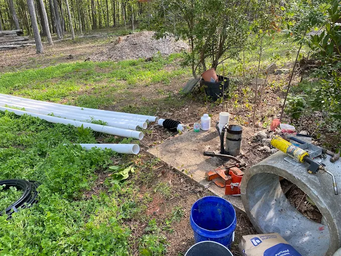 PVC drop pipe and tools staged at a wooded well site