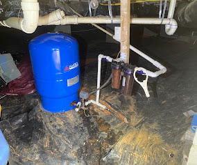 Blue pressure tank and dual sediment filters installed in a crawl space