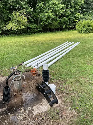New drop pipe and pitless equipment staged at a well on a green lawn